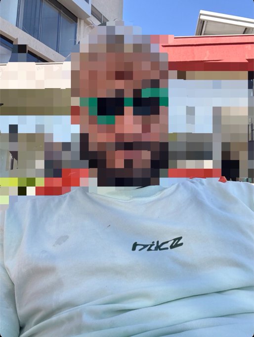 A person wearing a Nike shirt has their face pixelated into a Minecraft-style block texture with a beard and green eyes, matching the post's "gm face reveal but make it decentralized" caption by embracing a pixelated, crypto/blockchain aesthetic.