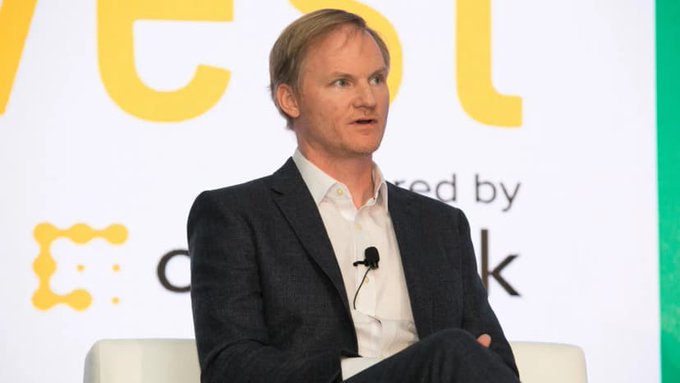 A man in a dark blazer speaks at a panel discussion, with partial text "ted by" and a logo visible behind him, likely related to a financial industry event.

The image appears to depict a business executive at a finance or fintech conference, though the speaker's identity isn't clearly confirmed. The context of the post about BitGo's acquisition of NYDIG's trading arm for $42.5M suggests this could be related to institutional crypto leadership, but the caption should focus only on what's visible: a suited speaker at an industry event.