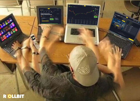 Viewed from behind, a person wearing a cap with a Bitcoin logo uses four laptops and a smartphone simultaneously, with the screens displaying crypto trading charts. The "ROLLBIT" logo appears in the bottom left corner.