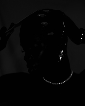 A dark, low-exposure portrait shows the silhouette of a person with water droplets on their face and shoulders, wearing a silver chain necklace.
