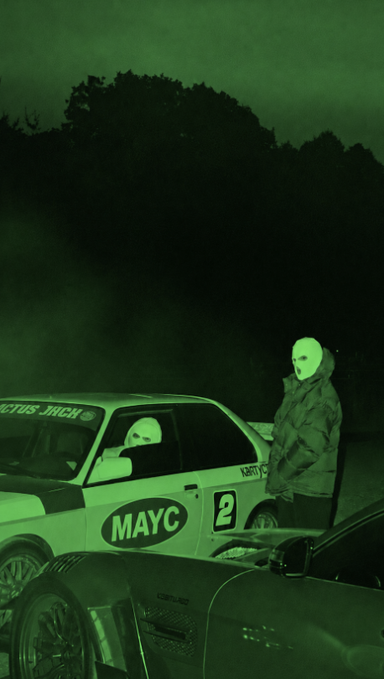 Two figures in white masks and hooded jackets stand beside a race car marked "MAYC" and the number "2" at night, bathed in an eerie green glow that gives the scene a mutant, post-apocalyptic feel—visually echoing the "Monday, mutated" caption. The mysterious, radioactive-toned atmosphere transforms an ordinary race setting into something otherworldly.