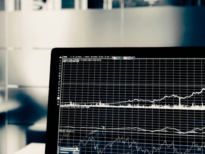 A close-up view of a laptop screen displaying multiple financial charts, graphs, and data visualizations on a dark background.