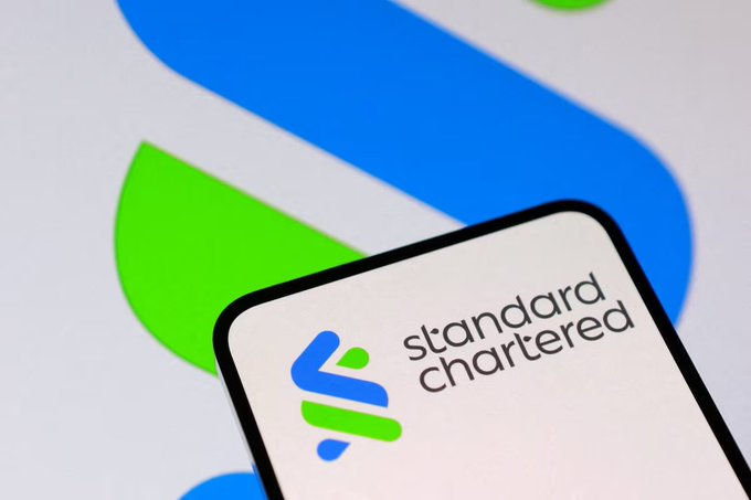A smartphone displaying the 'Standard Chartered' logo and text is positioned in front of a larger version of the same blue and green logo.