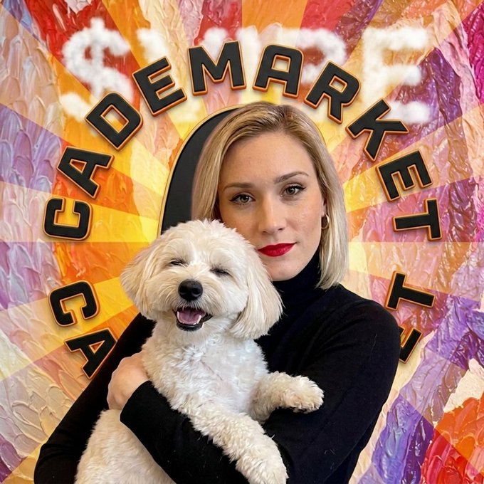 A woman with blonde hair and red lipstick holds a small white fluffy dog in front of a colorful psychedelic background featuring the stylized text "CAVENDEMARKET".
