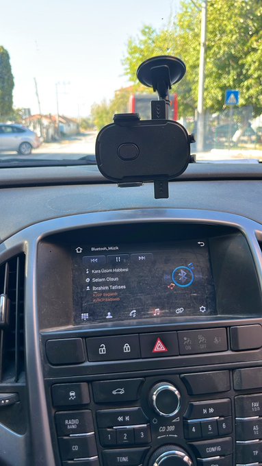 A phone mount is attached to a car dashboard above a media display playing "Bluetooth_Muzik" with tracks including "Euro Disco Halbeats" and "Oshun Olcum".
