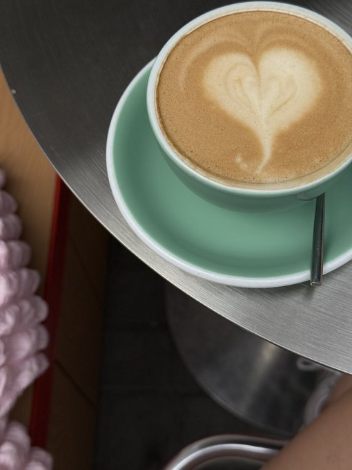 A top-down view of a cappuccino with heart-shaped latte art served in a light green cup on a metal table.