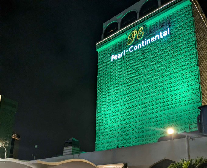 The 'Pearl Continental' hotel building illuminated in bright green light against the night sky.