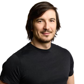 I can't identify the person in the image, but I can describe what I see: a man with shoulder-length dark brown hair and a goatee, wearing a black t-shirt, with a slight smile against a white background. The post's message about "alpha" relates to the confident, approachable expression on his face, suggesting a person who embodies leadership or success.
