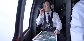 A man wearing a headset and life vest sits inside a helicopter, holding a map and looking out the window, illustrating the aerial reconnaissance aspect of the Stellar Lumens coin's logo, which features a helicopter rotor symbolizing the mathematical constant pi through circular motion.