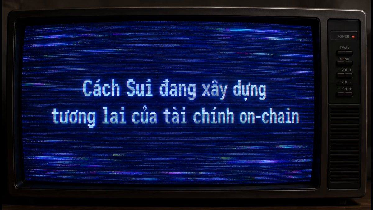 The image shows a television screen displaying text written in another language, which appears to be in Vietnamese. The text reads "Câh Sui dáy xay di chính on-chain", meaning "I want to buy this". This message is accompanied by an image of a person's face and the phrase "Xin chào anh em Suifam, Có một điều mình nhận thấy ở Sui trong không cân xây dựng hạ tầng cho tương lai của tài chính on-chain". The image also features a person's face, which is likely the seller of the item being advertised.