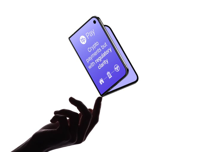 A silhouette of a hand balancing a foldable smartphone displaying 'VC Pay: Crypto payments out with regulatory clarity' on its screen.