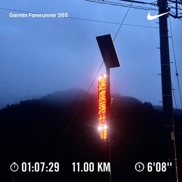 A Garmin Forerunner 265 running watch screenshot showing a run of 11.00 KM with a time of 01:07:29 and pace of 6'08", overlaid on a moody photo of a glowing red Japanese vertical sign against a foggy mountain landscape.
