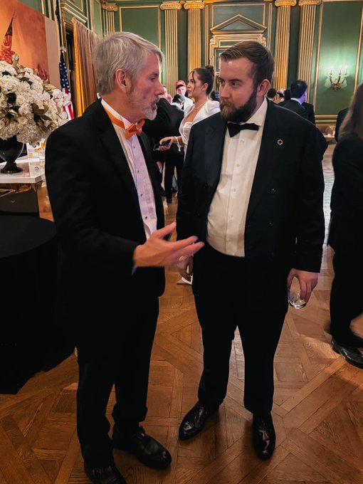 Two men in formal attire—one with a bow tie, the other with an orange bow tie—engage in conversation at an elegant reception, seemingly unaware of the crypto critique below. The post calls out Chainlink ($LINK) for broken promises about payment abstraction, staking updates, universal gas tokens, and various abandoned projects, suggesting the well-dressed attendees represent the polished facade of an industry built on unfulfilled promises.