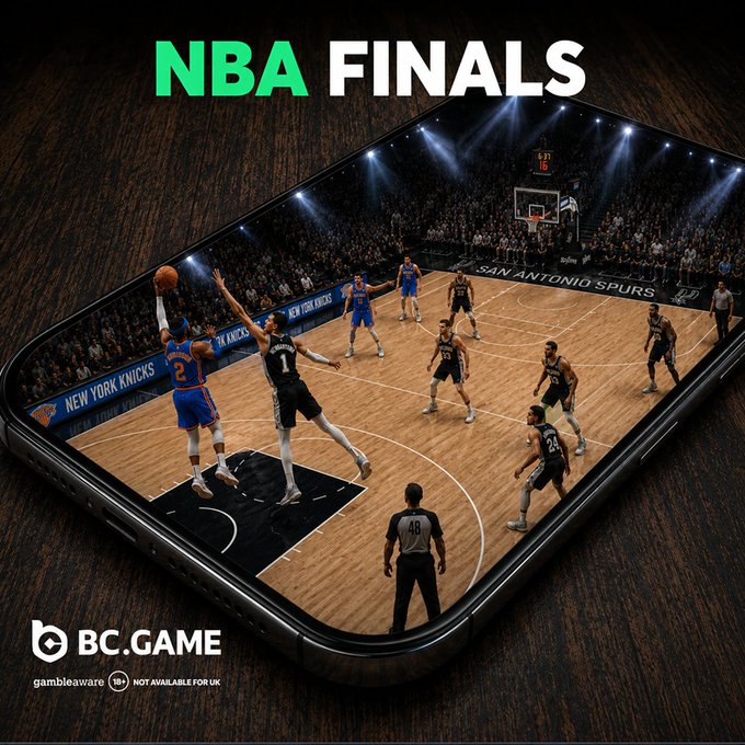 The image features a basketball game being played by two teams - the New York Knicks and the San Antonio Spurs. The players are actively engaged in the game, with one player jumping up to shoot the ball while another player attempts to block the shot. A referee is present on the court as well, ensuring that the game proceeds fairly.

The image also includes a cell phone placed near the center of the scene, which appears to be displaying the basketball game. The background of the image shows a wooden floor and a crowd watching the game from behind the players.