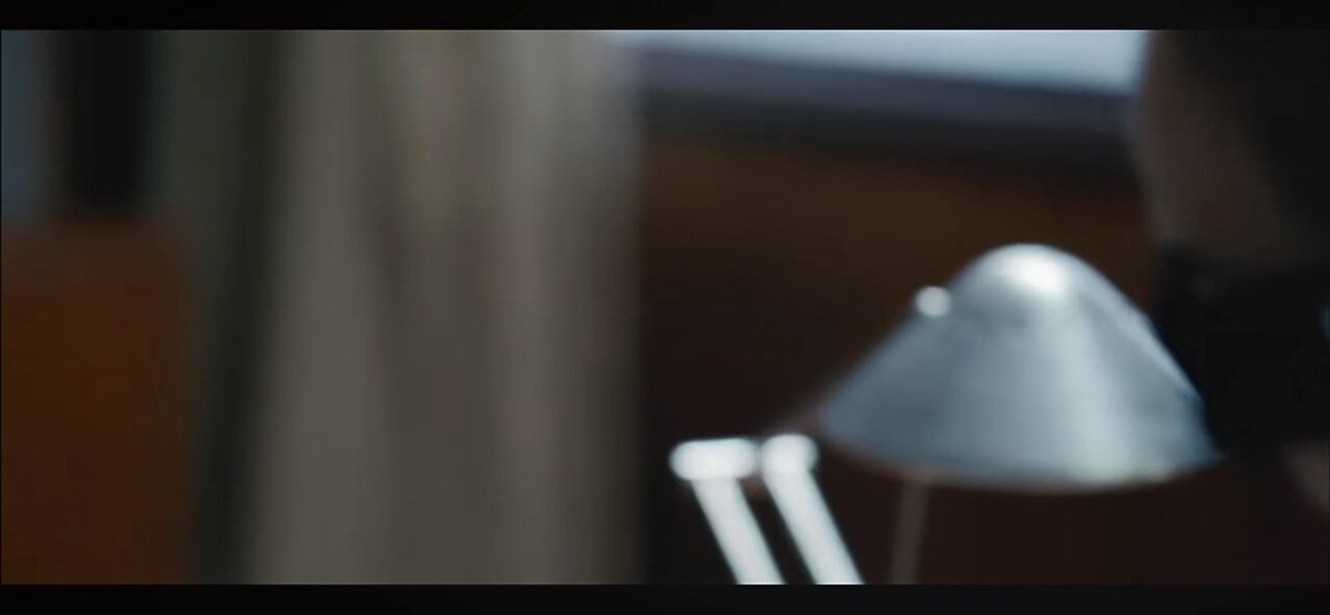 urn of water on a table, with a blurred reflection of the person holding it and a lamp casting light onto the surface.