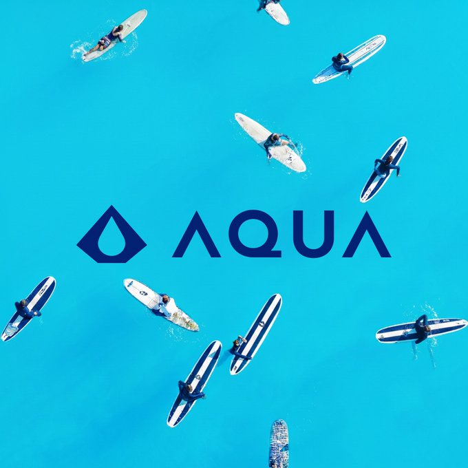An aerial view shows several people paddleboarding on bright turquoise water, with a dark blue 'AQUA' logo and water drop symbol overlaid in the center.