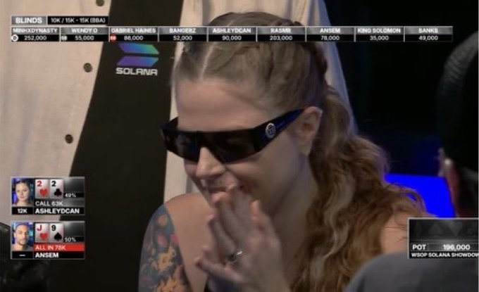 A screenshot from the WSOP Solania Showdown poker tournament featuring a woman with braided hair and sunglasses smiling, with on-screen graphics showing 'BLINDS 10K / 15K - 15K (BB)' and players 'ASHLEYDCAN' and 'ANSEM'.