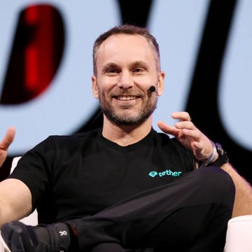 A smiling man wearing a black t-shirt with the "Tether" logo speaks on a stage, gesturing with his hand while wearing an earpiece microphone, representing the company behind the new peer-to-peer "Hypersearch" search engine.