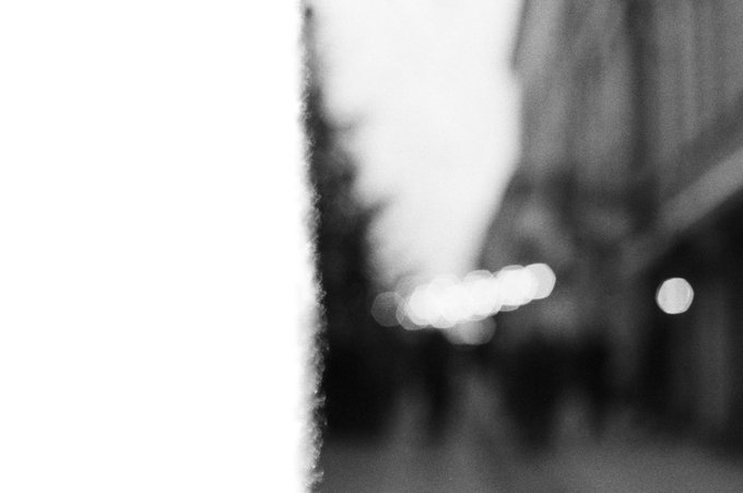 A blurry black and white photograph of a street scene with bokeh lights, featuring an overexposed white area on the left side.