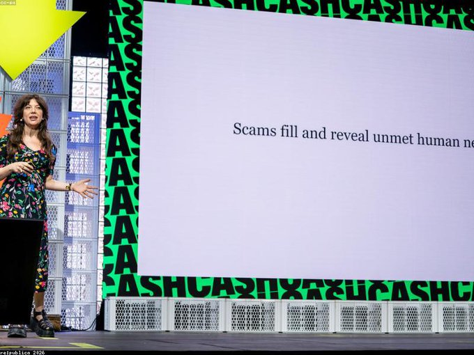 A woman in a floral dress stands on a stage presenting at re:publica 2026, with a slide reading 'Scams fill and reveal unmet human ne...' behind her and a green 'ASHCASH' patterned backdrop.