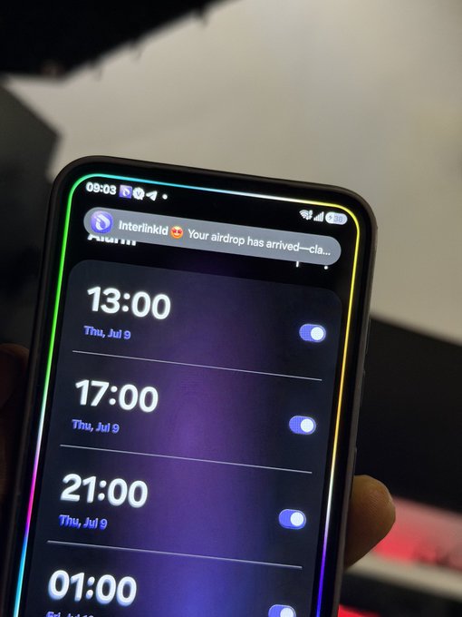 A close-up of a smartphone screen showing alarm times set for 13:00, 17:00, 21:00, and 01:00 on Thursday, July 9, with a notification from Interlinkid about an AirDrop arrival.