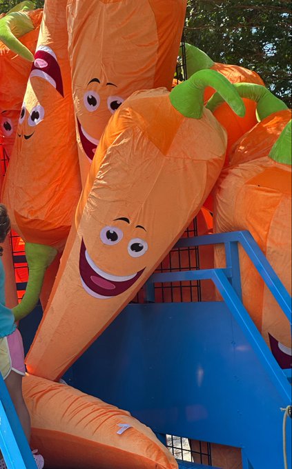 Several large inflatable carrots with smiling cartoon faces stacked together at what appears to be a fair or amusement park.