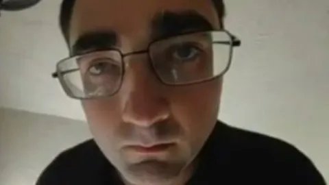 Close-up of a man wearing glasses looking into the lens.