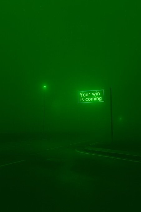 A moody, foggy nighttime street scene bathed in green light, featuring an illuminated sign that reads 'Your win is coming'.