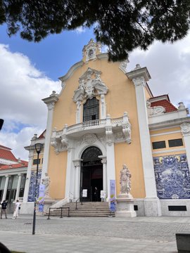 A yellow Baroque-style church or chapel facade with ornate white decorative elements, sculptures, and blue and white azulejo tile panels, photographed on a partly cloudy day.