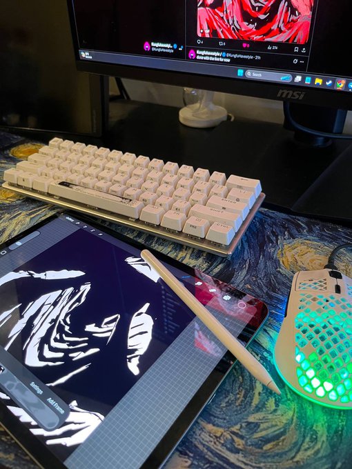 A desk setup featuring a white mechanical keyboard, a tablet displaying digital art with a stylus, a glowing RGB mouse on a patterned mat, and an MSI monitor in the background.