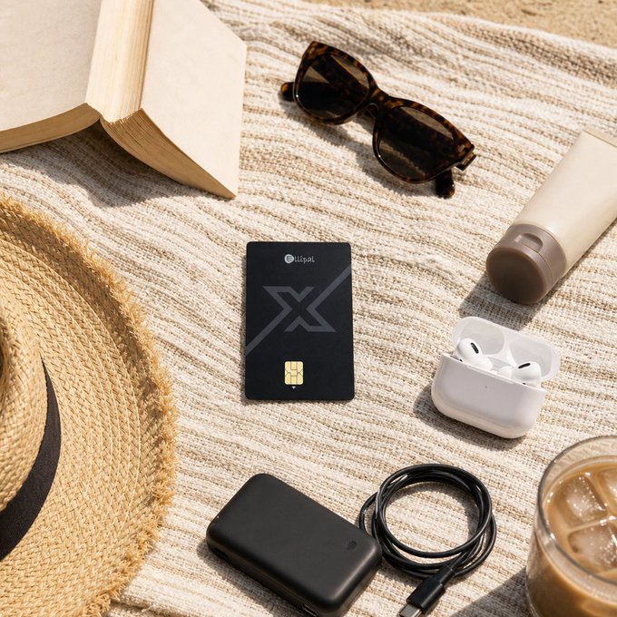 This image shows the "X Card" by Utripal alongside typical summer vacation items like a straw hat, sunglasses, and sunscreen, illustrating the card's suitability for travel and everyday use. The presence of a power bank and charging cable also hints at its compatibility with the "Cold Wallet Summer" theme mentioned in the post, which likely refers to keeping digital assets secure and accessible even while on vacation.