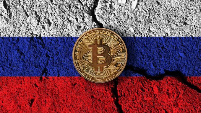 A gold Bitcoin coin mounted on a cracked wall painted with the white, blue, and red horizontal stripes of the Russian flag.