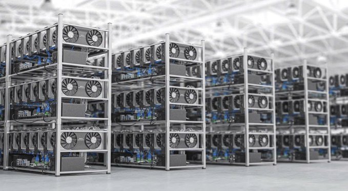 Rows of Bitcoin mining rigs with cooling fans arranged on metal racks inside a large warehouse facility, illustrating the digital infrastructure tied to the AI and Bitcoin mining industry highlighted in the post.
