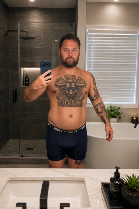 A shirtless, bearded man with a prominent "THE SILVER BULL" buffalo tattoo stands in a modern bathroom taking a mirror selfie with his phone, wearing Navy brand underwear. The image humorously reinforces the post's message about approaching a $100k market cap, with the "Silver Bull" tattoo serving as a visual pun on the bullish market sentiment being referenced.