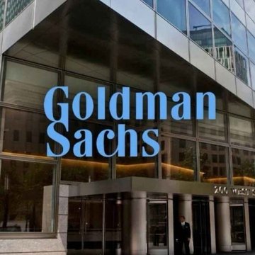The image displays the exterior of a Goldman Sachs building, with the company's iconic blue "Goldman Sachs" logo prominently featured on the glass facade. This visual ties directly to the news that Goldman Sachs, a $3.6T asset manager, is expanding into cryptocurrency by adding Bitcoin and Ethereum ETFs through its Neos acquisition.