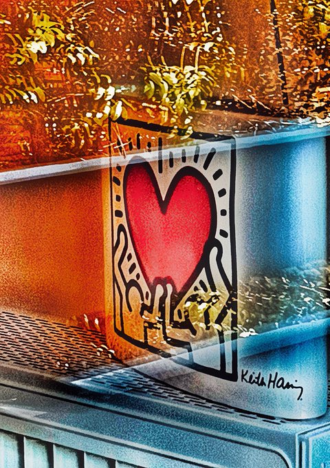A street art mural by Keith Haring depicting two hands cradling a red heart, painted on a weathered concrete ledge with golden autumn foliage above.