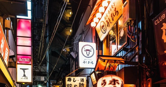 A vibrant nighttime street scene in Japan featuring illuminated neon signs, traditional lanterns, and Japanese text including "らぽっぽ" (Lapoppo), with a tall building displaying "CLUB" signage.