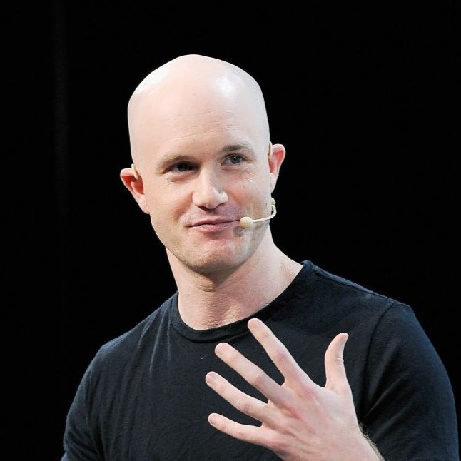 a bald man wearing a black shirt and headset microphone, smiling and gesturing with his hand against a black background