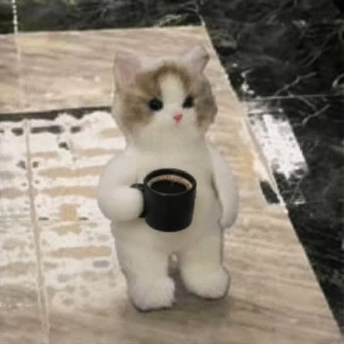 A plush toy of a small white and brown cat standing upright while holding a black coffee mug sits on a tiled floor.