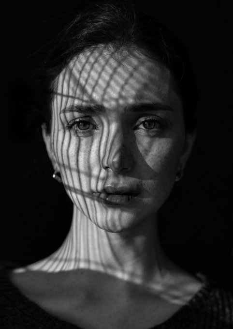A black and white artistic portrait of a young woman's face illuminated with geometric shadow lines.