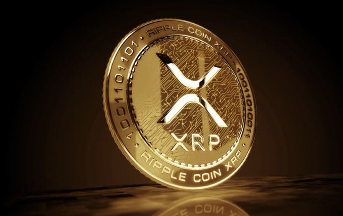 A gold Ripple Coin XRP token features the X logo with "RIPPLE COIN XRP" and binary patterns like "0001101101" around its edge, visually echoing the post's mention of $XRP trading at the $589 standard. The polished coin imagery reinforces the cryptocurrency being highlighted as meeting the noted price benchmark.
