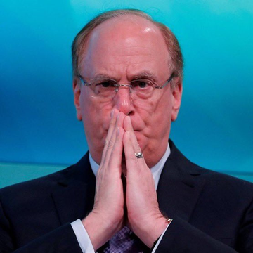 A portrait of an older man wearing glasses and a dark suit, with his hands clasped together near his face, appearing to be at a formal event.