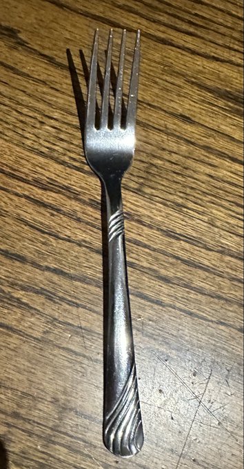 A metal fork with four tines resting on a wooden surface.