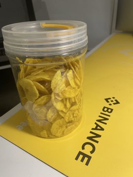 A clear plastic container filled with cereal flakes rests on a yellow Binance-branded laptop.