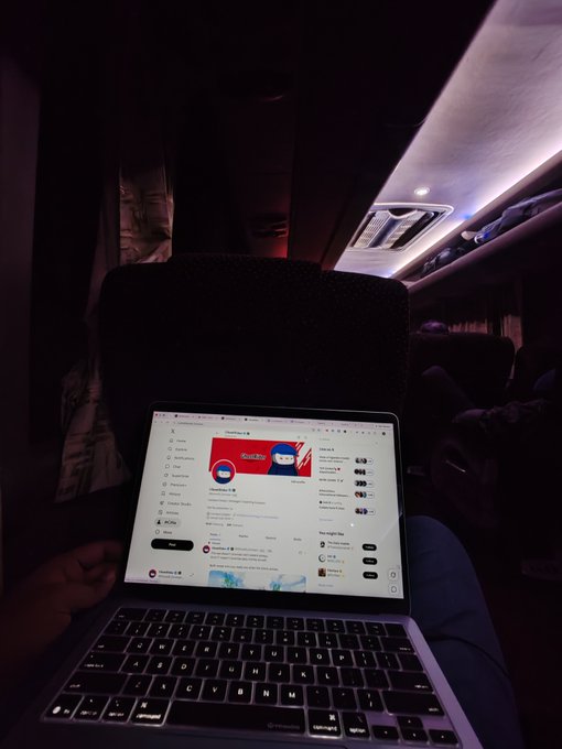 A first-person perspective photo taken in a darkened setting, likely an airplane cabin, showing a person's hand using a laptop displaying the YouTube homepage.