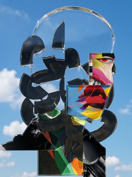 An abstract 3D artwork or sculpture with glossy black geometric shapes and colorful, distorted facial features (eye, red lips) set against a blue sky with clouds.