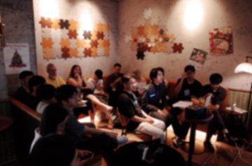 A dimly lit room with a group of people gathered, some holding plates and chatting, with decorative leaf artwork on the walls.