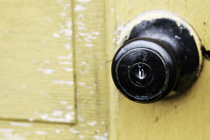 A close-up photograph shows a worn black doorknob mounted on a distressed yellow painted wooden door.