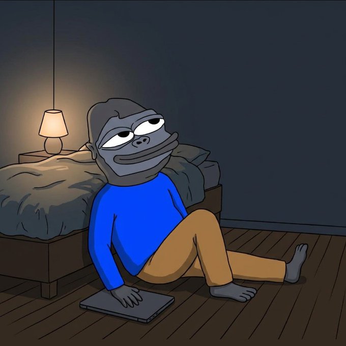 A cartoon frog character in a blue shirt and tan pants sits on a wooden floor beside a bed, holding a laptop with a tired expression under a warm bedside lamp.