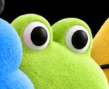 A close-up of a green Cookie Monster plush toy with large googly eyes next to a blue plush.